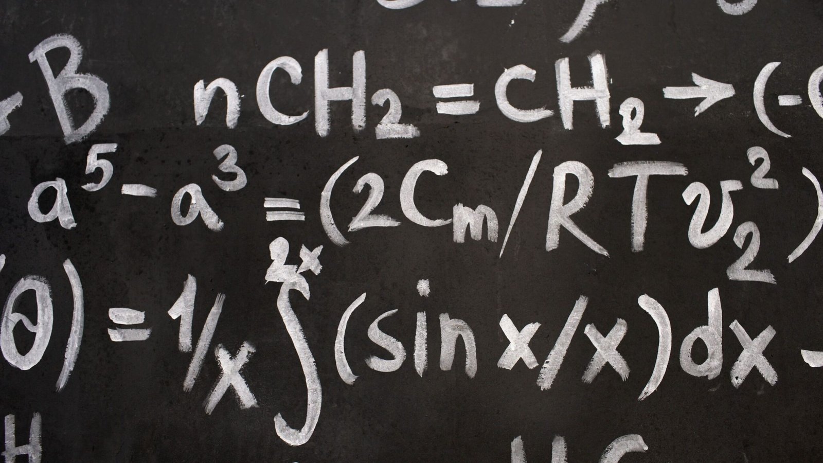 Close-up of complex equations on a chalkboard, showcasing chemistry and math symbols.